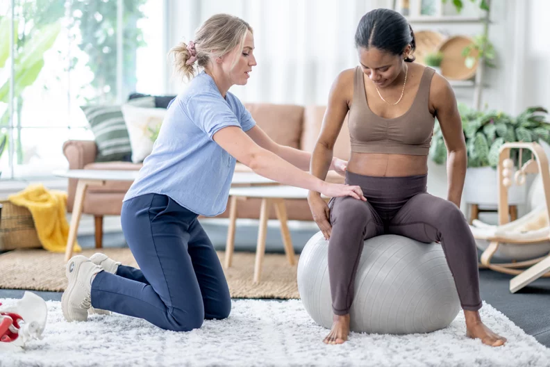 Een kinesitherapeut helpt een vrouw bij bekkenbodemtherapie met behulp van een oefenbal, illustrerend hoe deze therapie nuttig kan zijn voor verschillende patiëntgroepen zoals vrouwen na de bevalling en mensen met chronische bekkenpijn